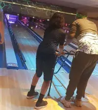 A teenager helping a young adult at bowling 
